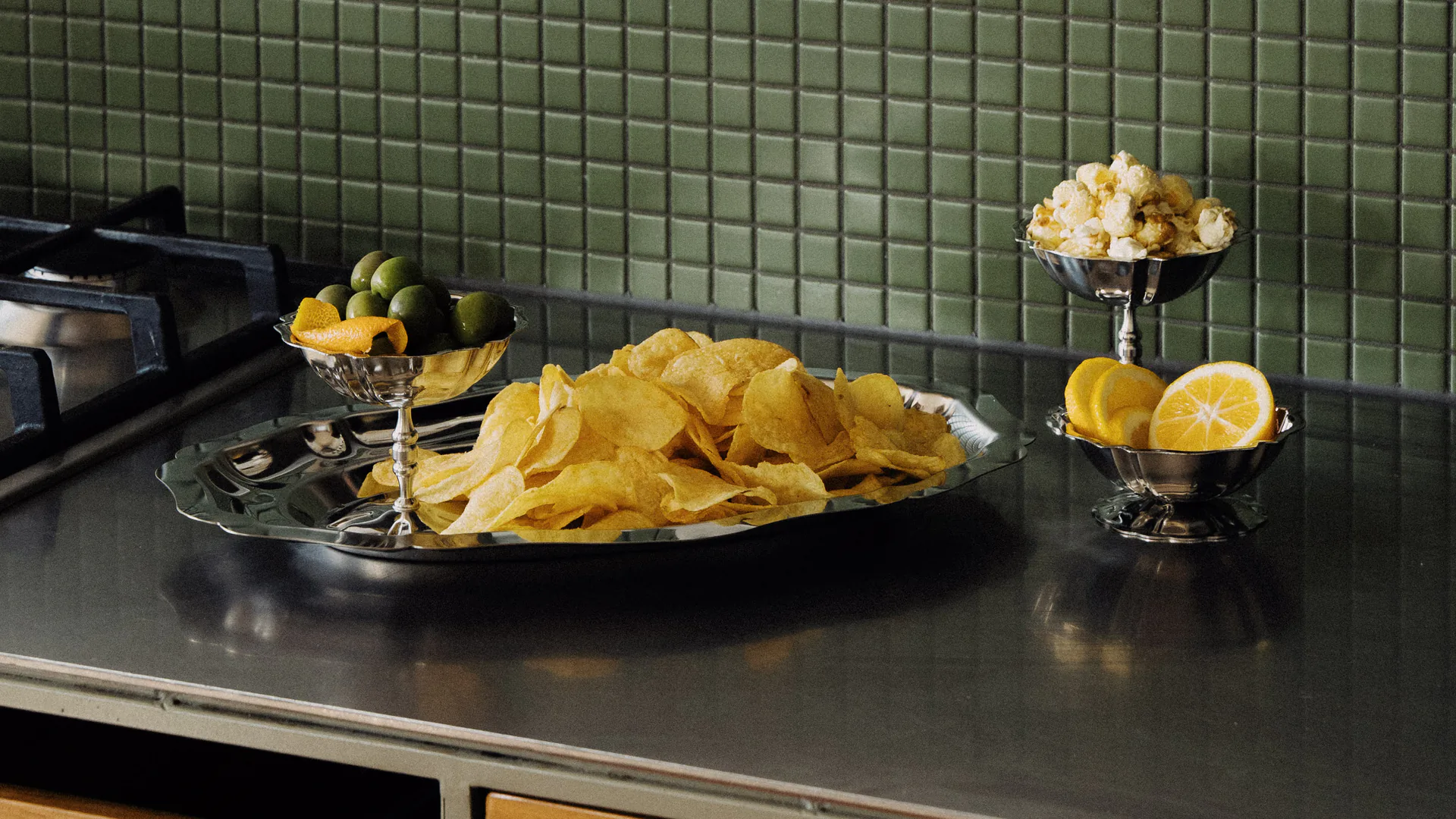 Silver serving dishes filled with potato chips, citrus and olives