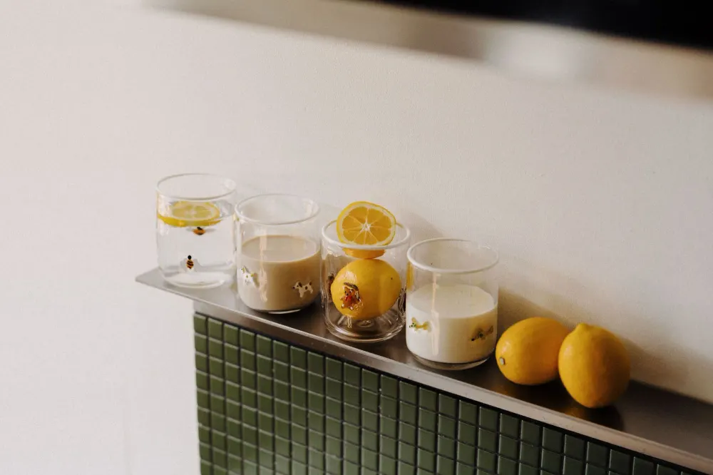 Four Icon Cups filled with water, milk and lemons on a steel shelf above green tiles
